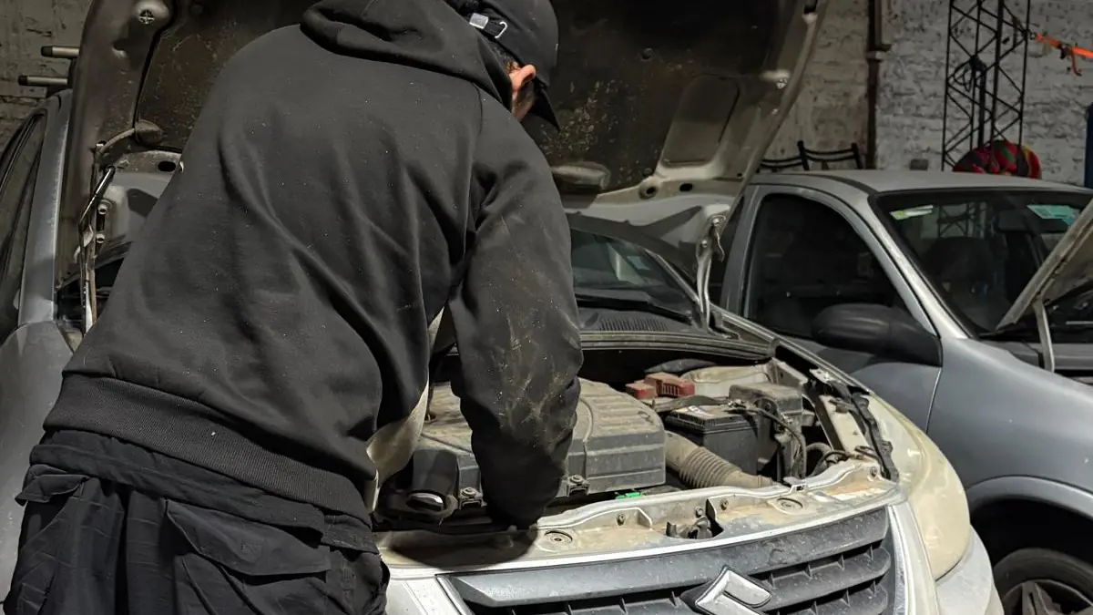 Mecánico de Automotora Sucre inclinado sobre el motor de un Suzuki con el capó abierto.