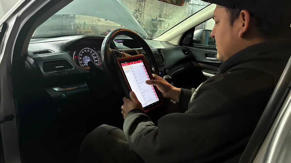 Mecánico leyendo los códigos del scanner en una tablet, sentado al volante del auto.