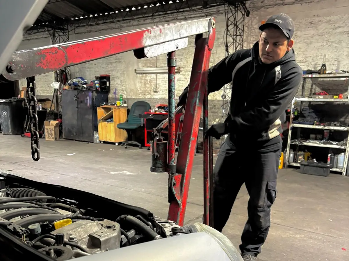 Mecánico de Automotora Sucre junto a la grúa de motor, con un auto abierto en el box del taller.
